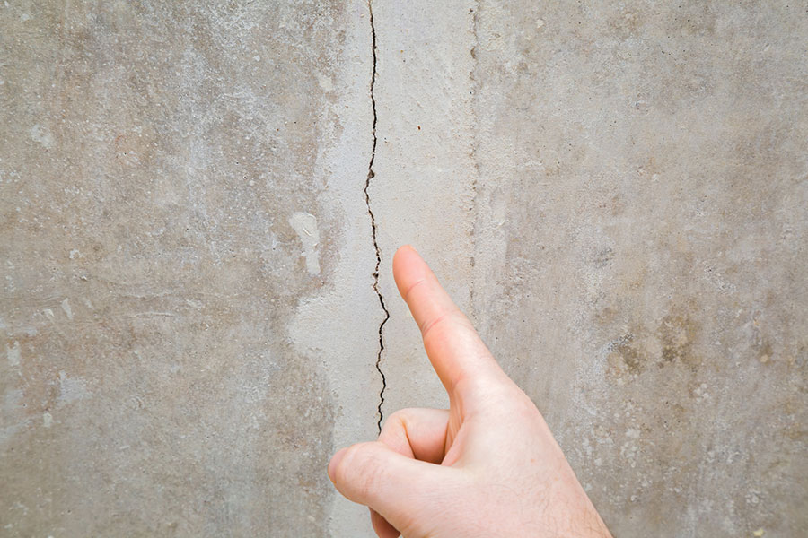 A hand points at a vertical crack running through a concrete wall, highlighting damage and the need for foundation crack repair in New Baltimore MI. A hand points at a vertical crack running through a concrete wall, highlighting damage and the need for foundation crack repair in New Baltimore MI.
